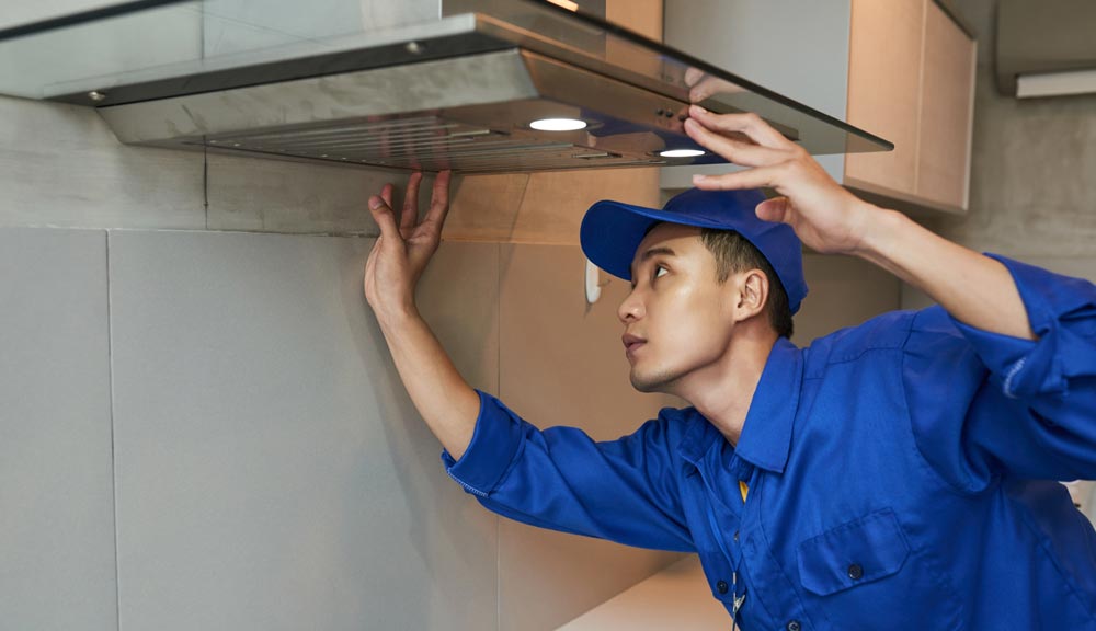 Professional cleaner removing grease from a kitchen exhaust hood in Downtown Dubai.