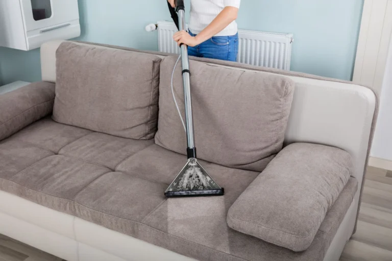 A professional upholstery cleaner uses a vacuum extraction tool to remove deep-seated stains and grime from a fabric sofa.